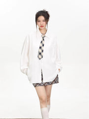 Model wearing an oversized white collared shirt with a checkered tie and a brown and grey plaid mini skirt.