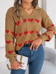 Woman holding a white clutch and wearing a tan knit sweater with red heart pattern and blue jeans