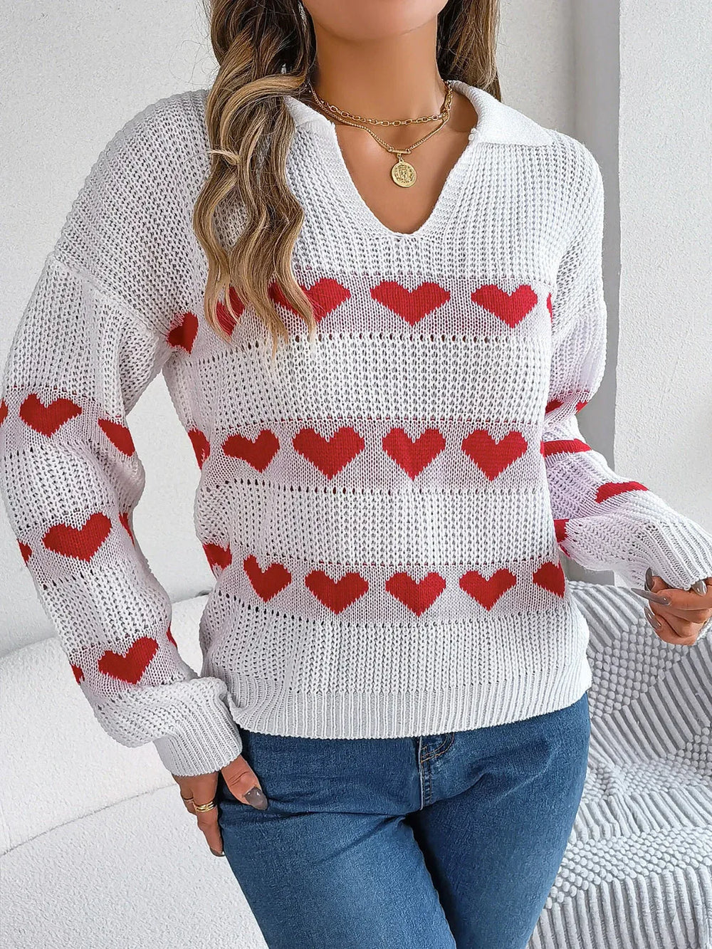 Woman wearing a white knit sweater with red heart pattern and blue jeans