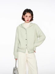 Woman wearing a light green hooded cardigan with white pants and a silver bag, front view