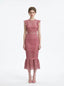 Woman wearing a pink lace dress with ruffled cap sleeves and a mermaid hemline, front view.