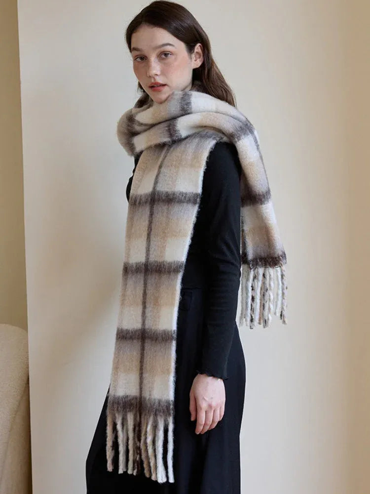 Profile view of a woman wearing a black top and pants, with a voluminous plaid scarf draped over her shoulders and neck.