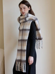 Profile view of a woman wearing a black top and pants, with a voluminous plaid scarf draped over her shoulders and neck.