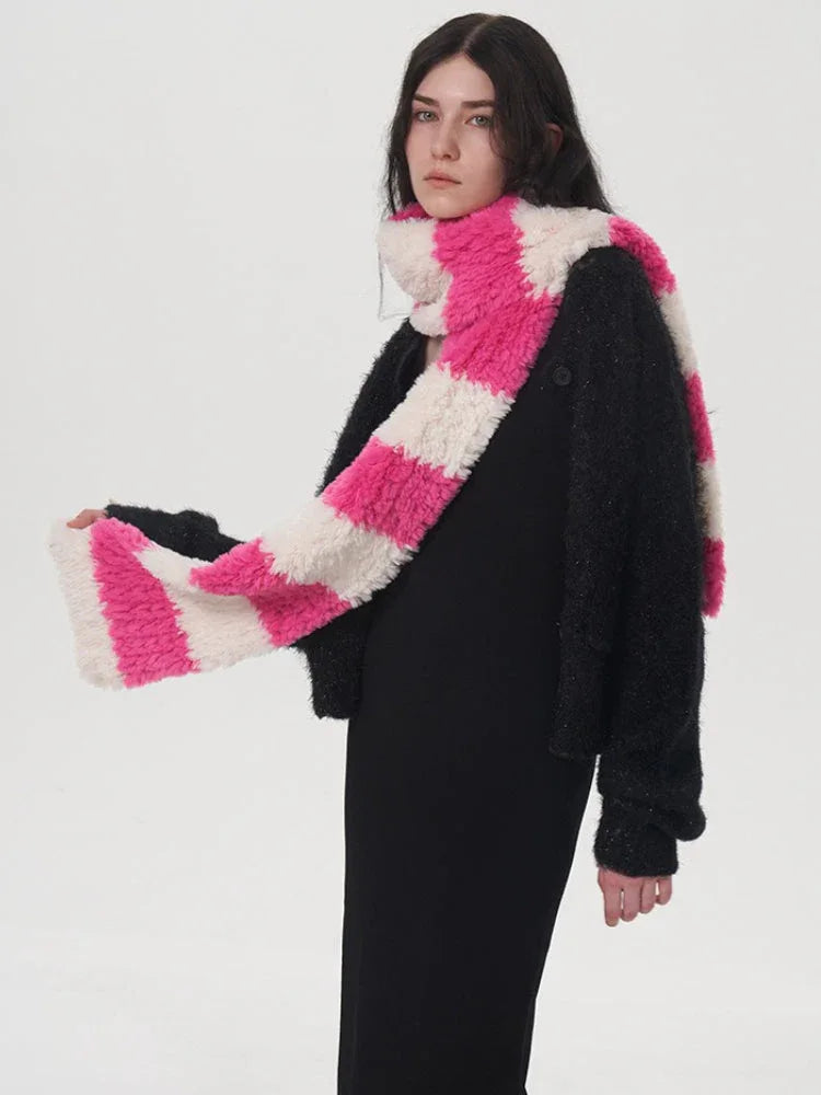 Model adjusting a pink and white striped fuzzy scarf worn with a black sweater and black dress.