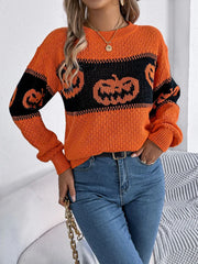 Close-up of a woman's torso wearing an orange and black pumpkin print knit sweater and blue jeans