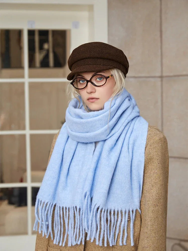 Close-up of a young woman's face, wearing a light blue fringed scarf and round glasses.