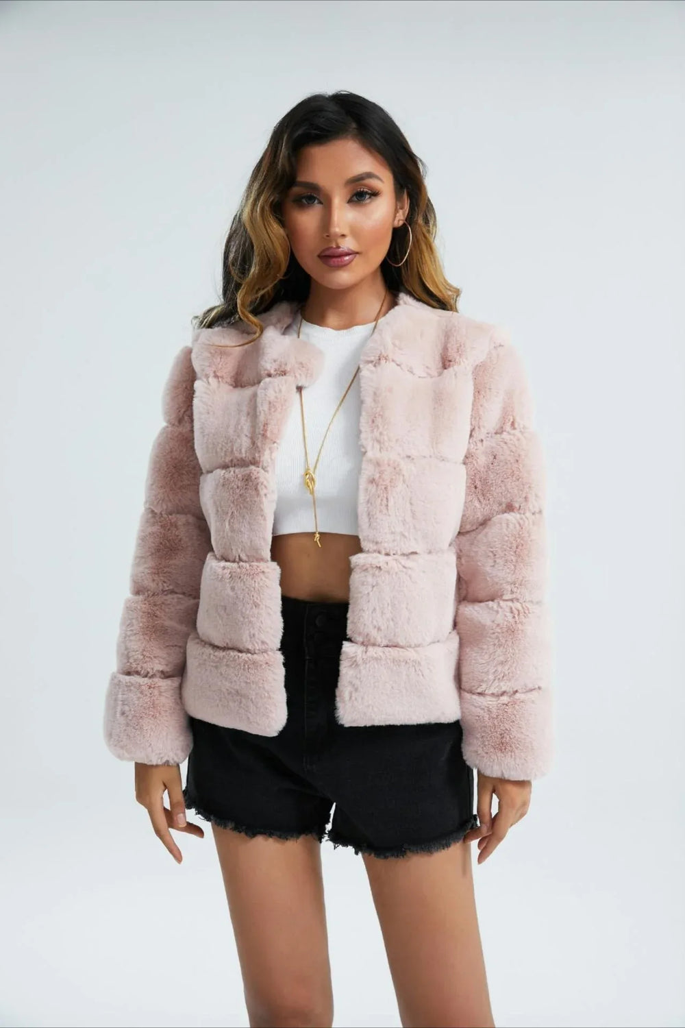 Woman wearing a pink faux fur cropped jacket, hands clasped in front.