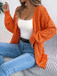 Woman wearing an orange open-front knit cardigan over a white tank top and blue jeans.