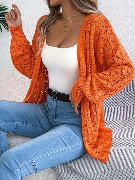 Woman wearing an orange open-front knit cardigan over a white tank top and blue jeans.