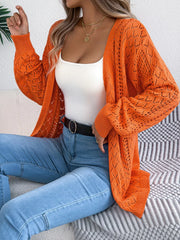 Woman wearing an orange open-front knit cardigan over a white tank top and blue jeans.