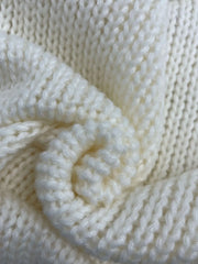 Detailed texture of the cream chunky knit fabric of the sweater.