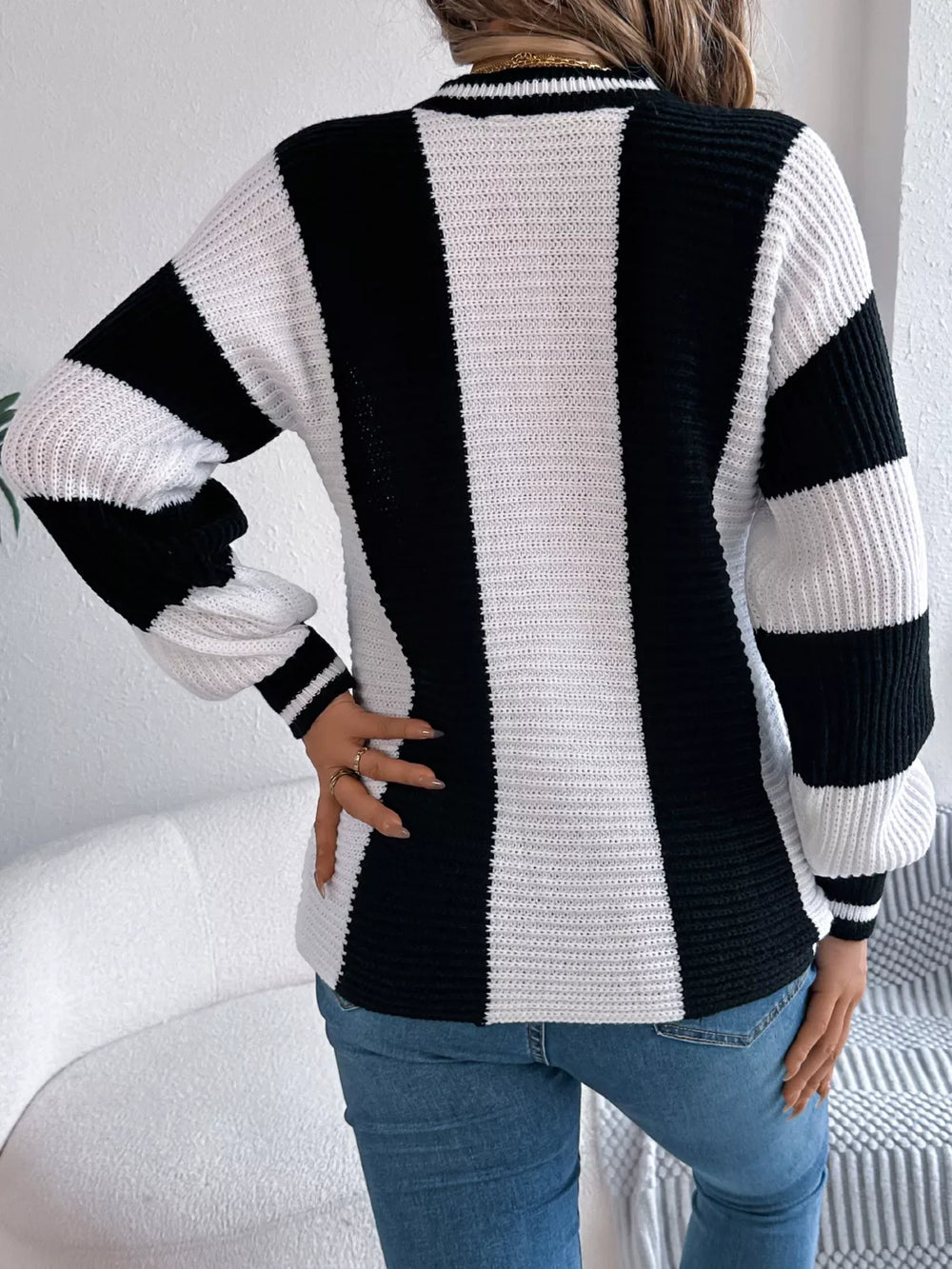Woman wearing a black and white striped knit sweater with blue jeans, back view.