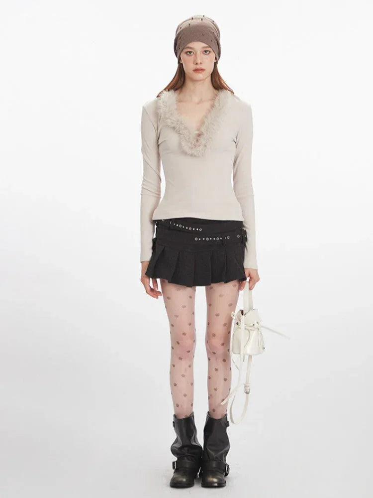 Woman wearing a cream long-sleeve top with fur trim, a black pleated mini skirt, decorative tights, and black boots, holding a white bucket bag.
