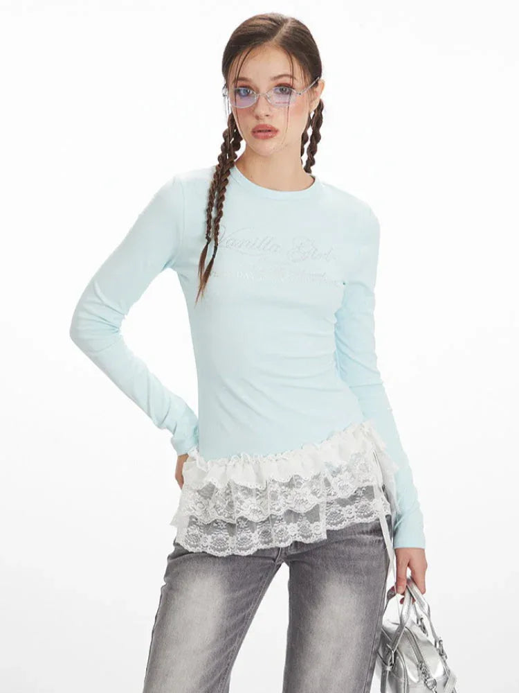 Front view of a woman wearing a light blue long-sleeve top with white lace trim and grey wide-leg jeans, posing with her hand on her hip.