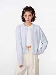 Woman wearing a light blue cropped knit cardigan over a white crop top and cream wide-leg pants.