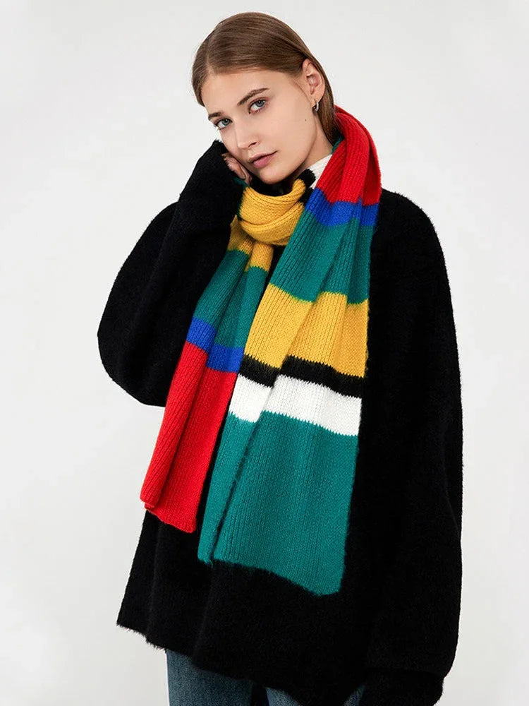 Woman touching her face while wearing a black sweater and a multicolored striped knit scarf