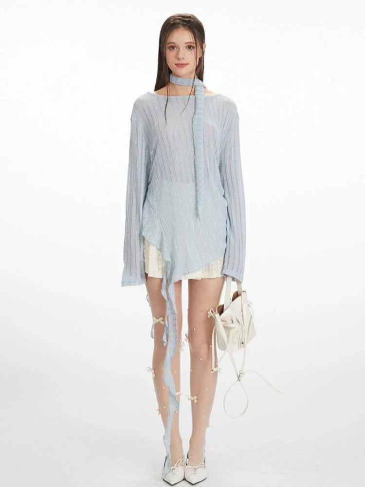 model wearing a light blue sheer knit sweater with an asymmetrical hem and a neck scarf, paired with a white lace skirt and white heels, holding a white handbag