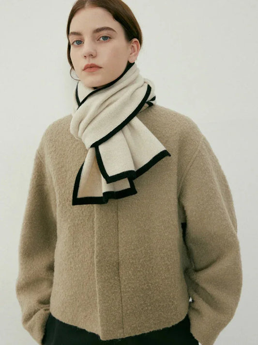 Woman wearing a beige textured coat and a cream scarf with black trim
