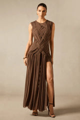 Model wearing a brown sleeveless maxi dress with a high slit and intricate ruching detail on the bodice.