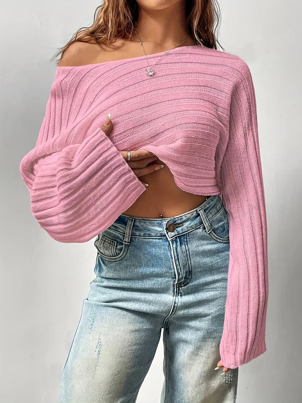 Woman wearing a pink cropped knit sweater off the shoulder, revealing her midriff and a belly piercing.