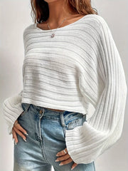 Woman wearing a white cropped knit sweater with bell sleeves and blue jeans.