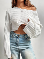 Woman wearing a white cropped knit sweater off the shoulder, revealing her midriff and a belly piercing.