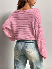 Back view of a woman wearing a pink cropped knit sweater with bell sleeves and distressed blue jeans.