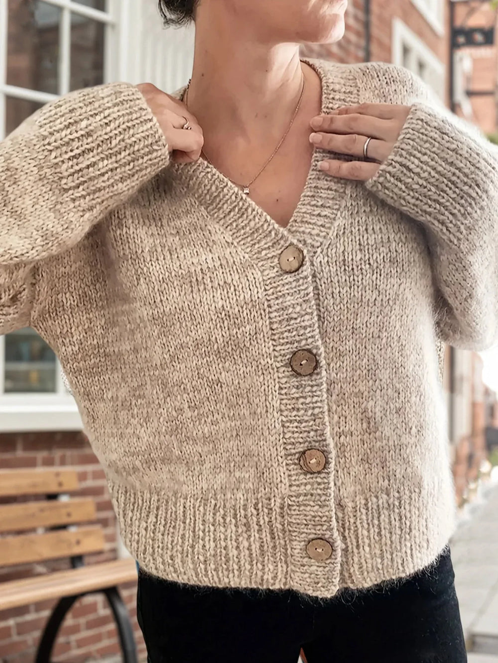 Woman wearing a beige chunky knit cardigan with a V-neck and wooden buttons.