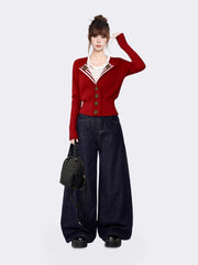 Full body shot of a woman in a red knit cardigan, white t-shirt, and dark wash wide-leg jeans, holding a black backpack