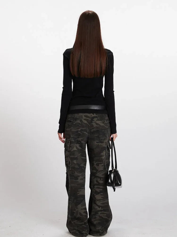 Back view of a woman in a black long-sleeve top and camouflage cargo pants, holding a black handbag.
