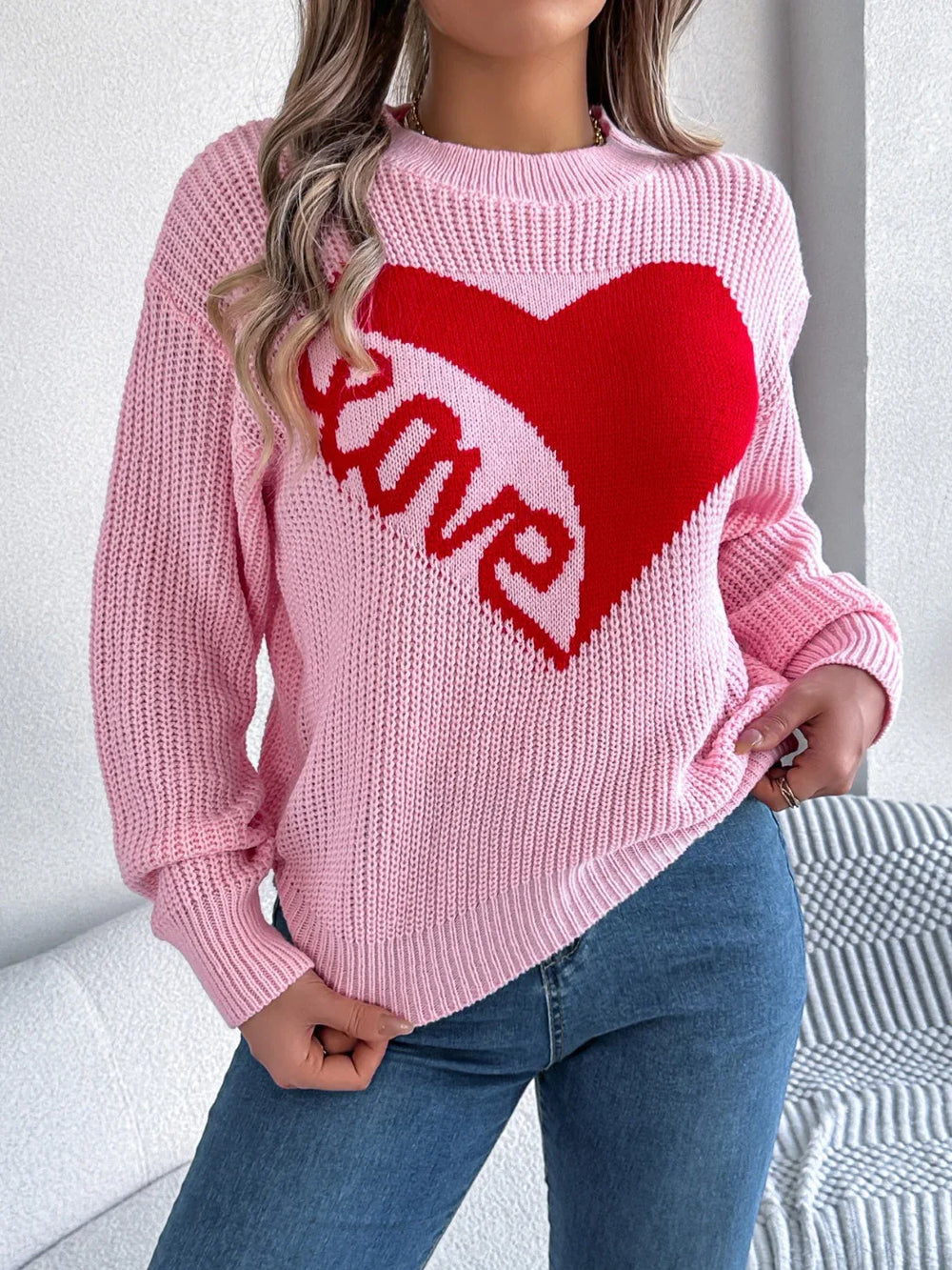 Front view of a woman wearing a pink knit sweater with a red heart graphic and the word "love" on the front.