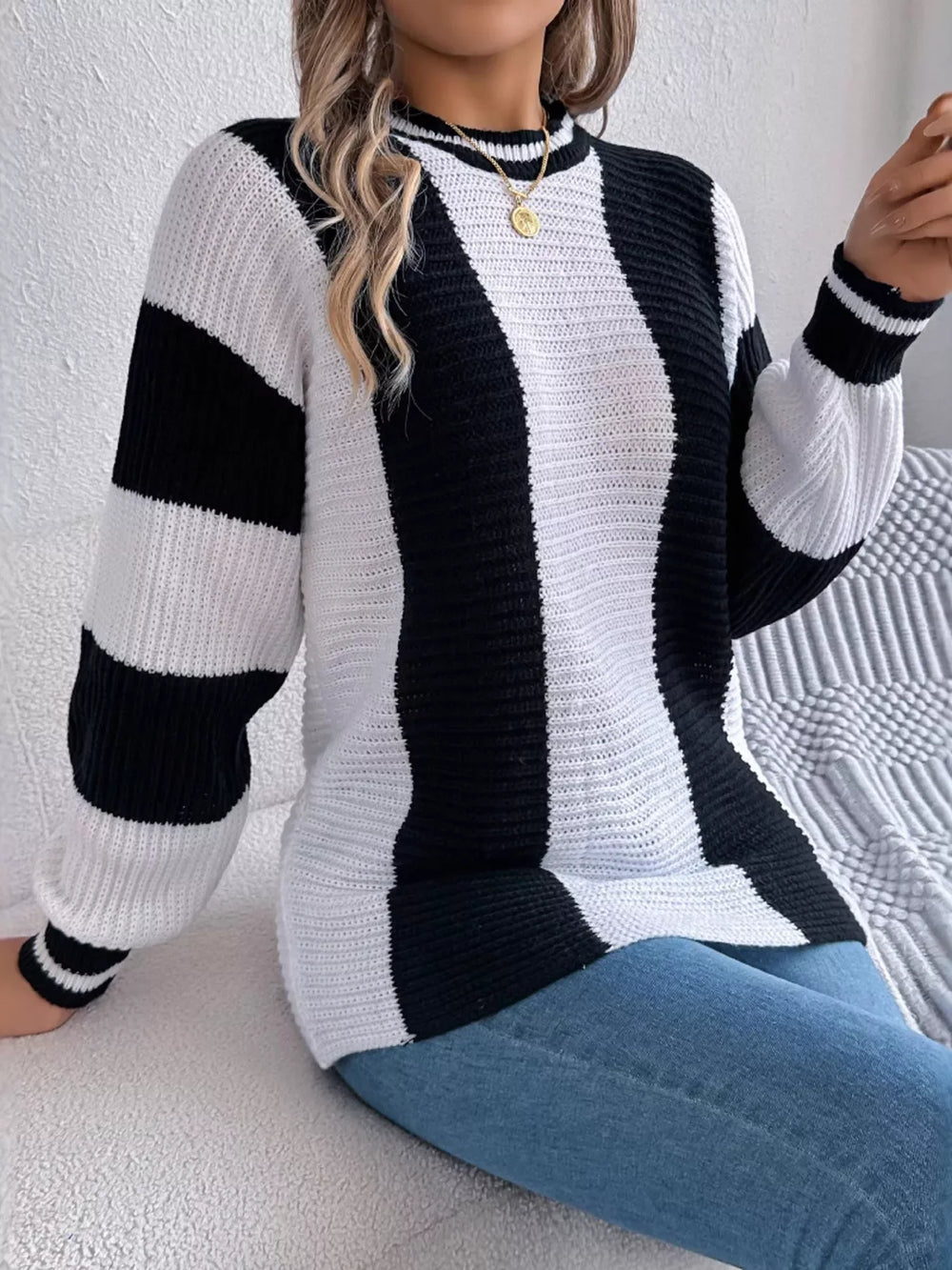 Woman wearing a black and white striped knit sweater and blue jeans, sitting on a couch.