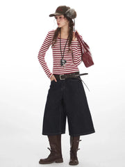Woman in a red and white striped long-sleeved shirt, dark wash wide-leg cropped jeans, brown belt, brown boots, and fur-trimmed hat, holding a red handbag.