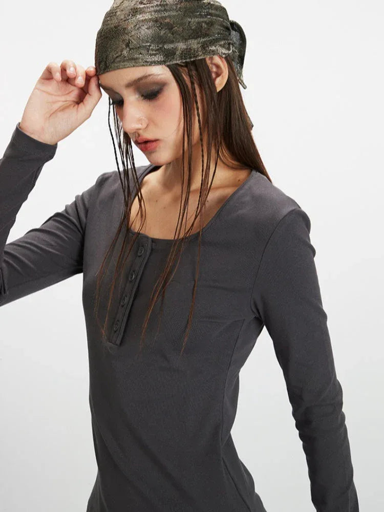 Close-up side view of a woman's upper body wearing a dark grey long-sleeve top with a square neckline and button details. She is wearing a patterned headscarf.