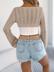 Back view of a woman wearing a beige cropped knit sweater with a white camisole and denim shorts