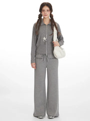 Woman wearing a grey knit zip-up jacket and wide-leg pants with a white shoulder bag.