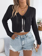 Woman wearing a black cropped knit cardigan with a tie front closure and denim shorts, holding a white handbag.