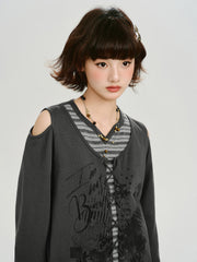 Close-up of the model's face and upper body, showcasing the layered grey top with graphic print and necklace.