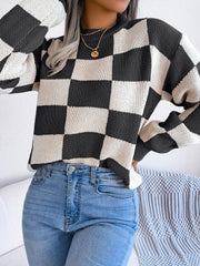 Woman wearing a black and white checkerboard knit sweater with light wash jeans, hands on hips, front view.