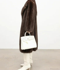 Side view of a woman in a brown mink fur coat, holding a white handbag.
