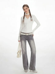 Full-length shot of a model in a white long-sleeved ribbed V-neck top and grey flared jeans.