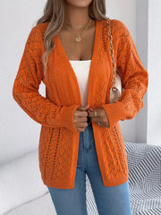 Woman adjusting an orange open-front knit cardigan, revealing a white tank top and blue jeans.