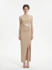 A woman models a shimmering champagne halter neck maxi dress with a cut-out and high slit.