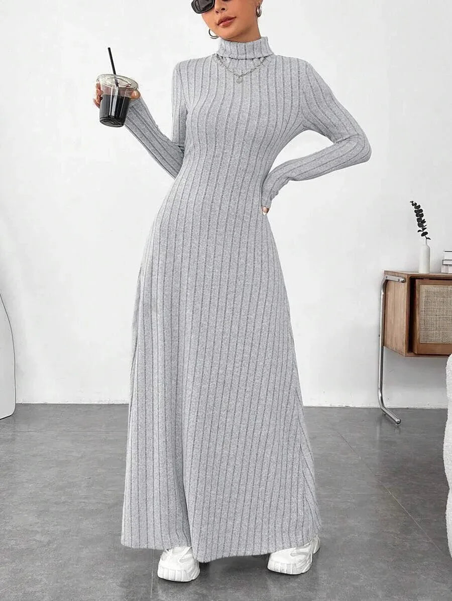 Woman wearing a grey ribbed knit maxi dress with a turtleneck and long sleeves, holding a drink.