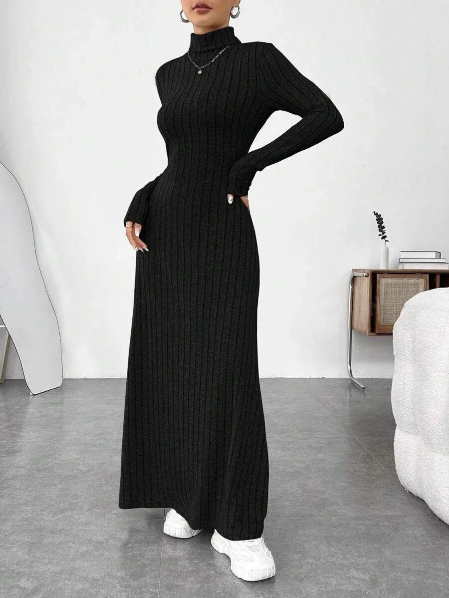 Woman wearing a black ribbed knit maxi dress with a turtleneck and long sleeves, posing with hands on hips.