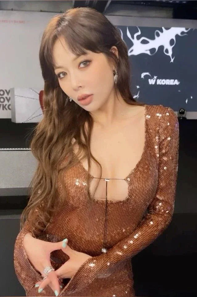 Close-up of a woman's face and upper body wearing a brown sequined dress with a plunging neckline and long sleeves.