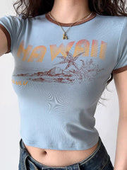 Close-up of a light blue cropped t-shirt with a "Hawaii" graphic print and brown trim.