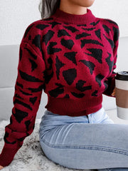 Woman sitting on a rug, wearing a red and black leopard print cropped knit sweater, light wash jeans, and holding a coffee cup.
