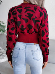 Back view of a woman in a red and black leopard print cropped knit sweater and light wash jeans.