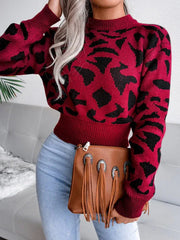 Woman wearing a red and black leopard print cropped knit sweater with light wash jeans and a brown fringe clutch.